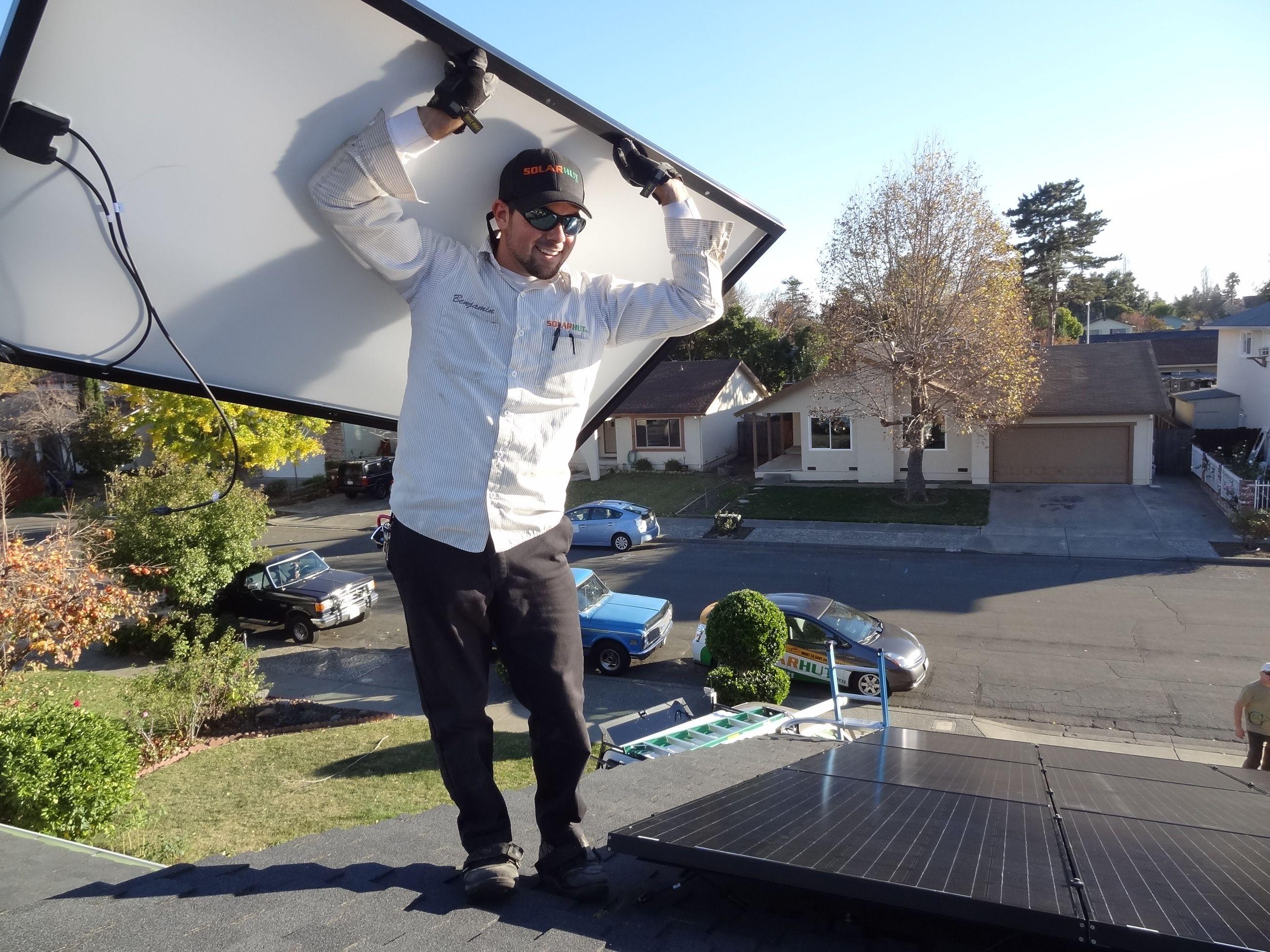 Technician carrying solar panel up on a roof