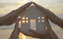 Hands Supporting a Paper Model of a House